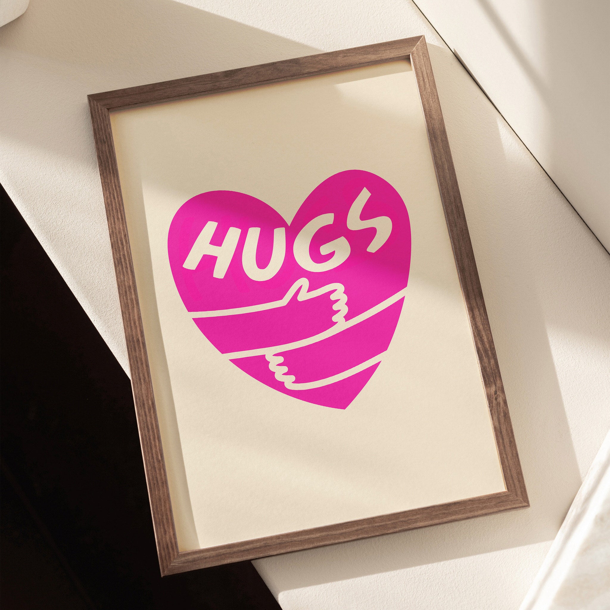 Vibrant pink heart poster with arms embracing and 'Hugs' text on a beige canvas
